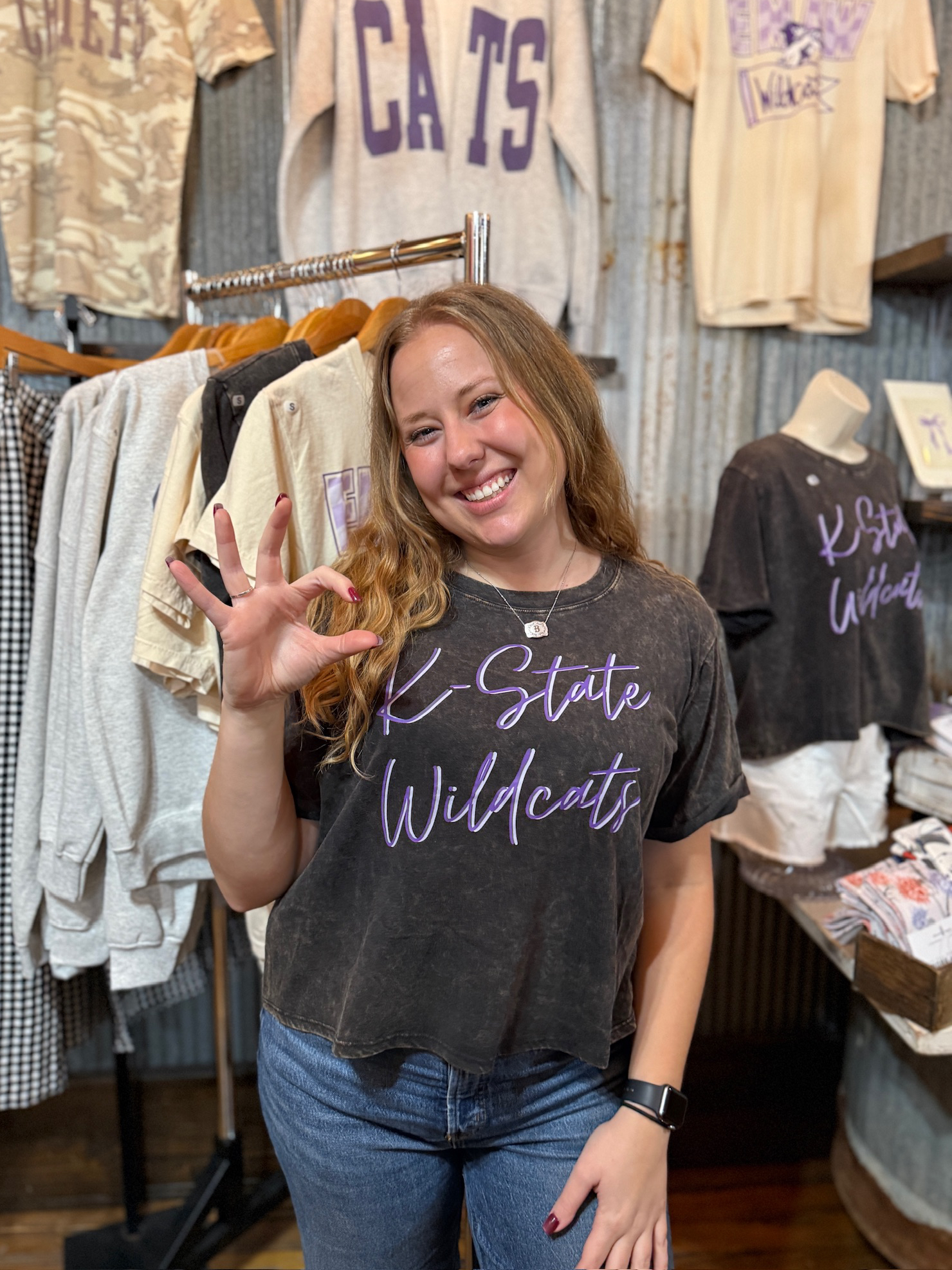 Woman wearing a mineral-wash black K-State Wildcats long crop graphic tee with lavender script.