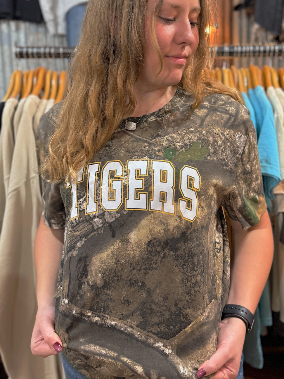 Close-up of a model wearing a Realtree camo Tigers tee showing the white and gold block lettering across the chest.