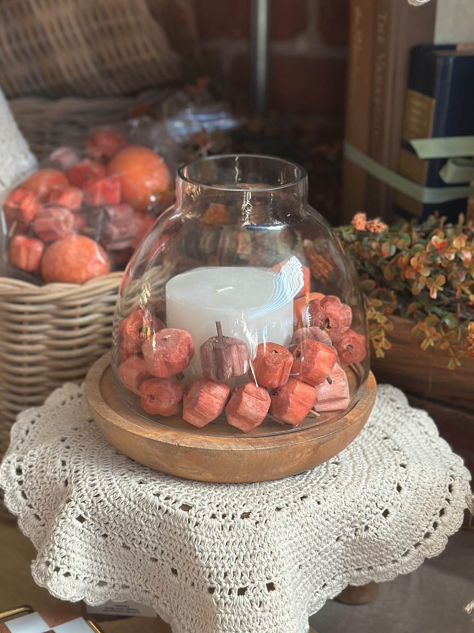 Pumpkin Shaped Mix Bowl Filler styled around a white pillar candle inside a wood and glass hurricane on a cream lace doily.