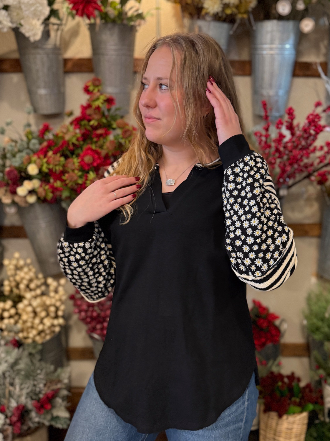 Woman wearing the black split-neck top with floral and stripe statement sleeves in a relaxed, oversized fit.