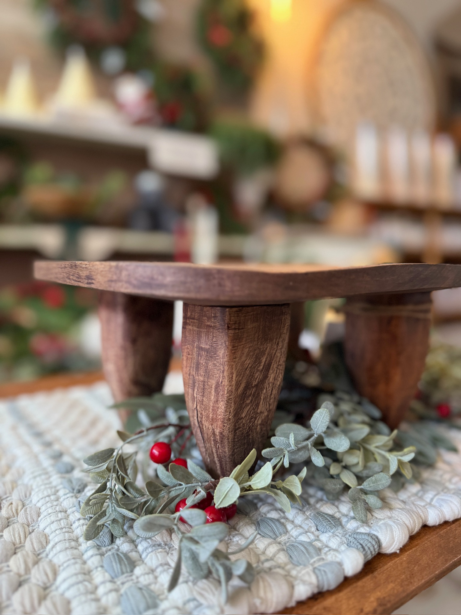 Square Wood Primitive Stool displayed on top of greenery and red berries, photographed from an angled corner view.