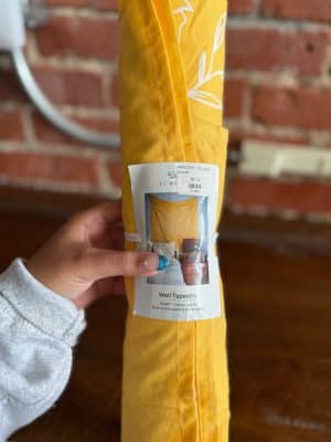 Yellow Wall Tapestry in packaging with product label, cotton fabric with white line accents.