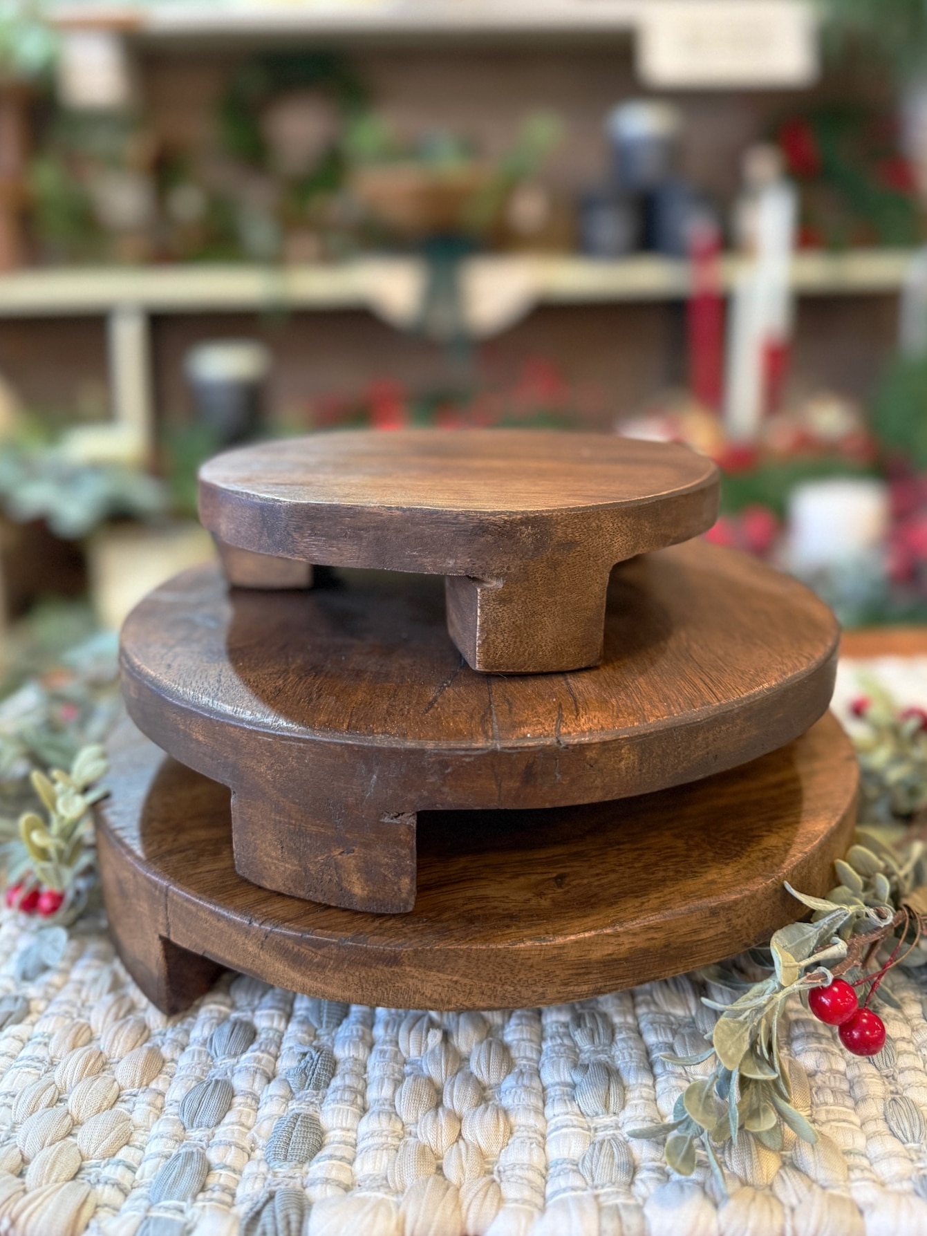 Stacked set of three found wood pedestals in varying sizes displayed on a woven mat with greenery.