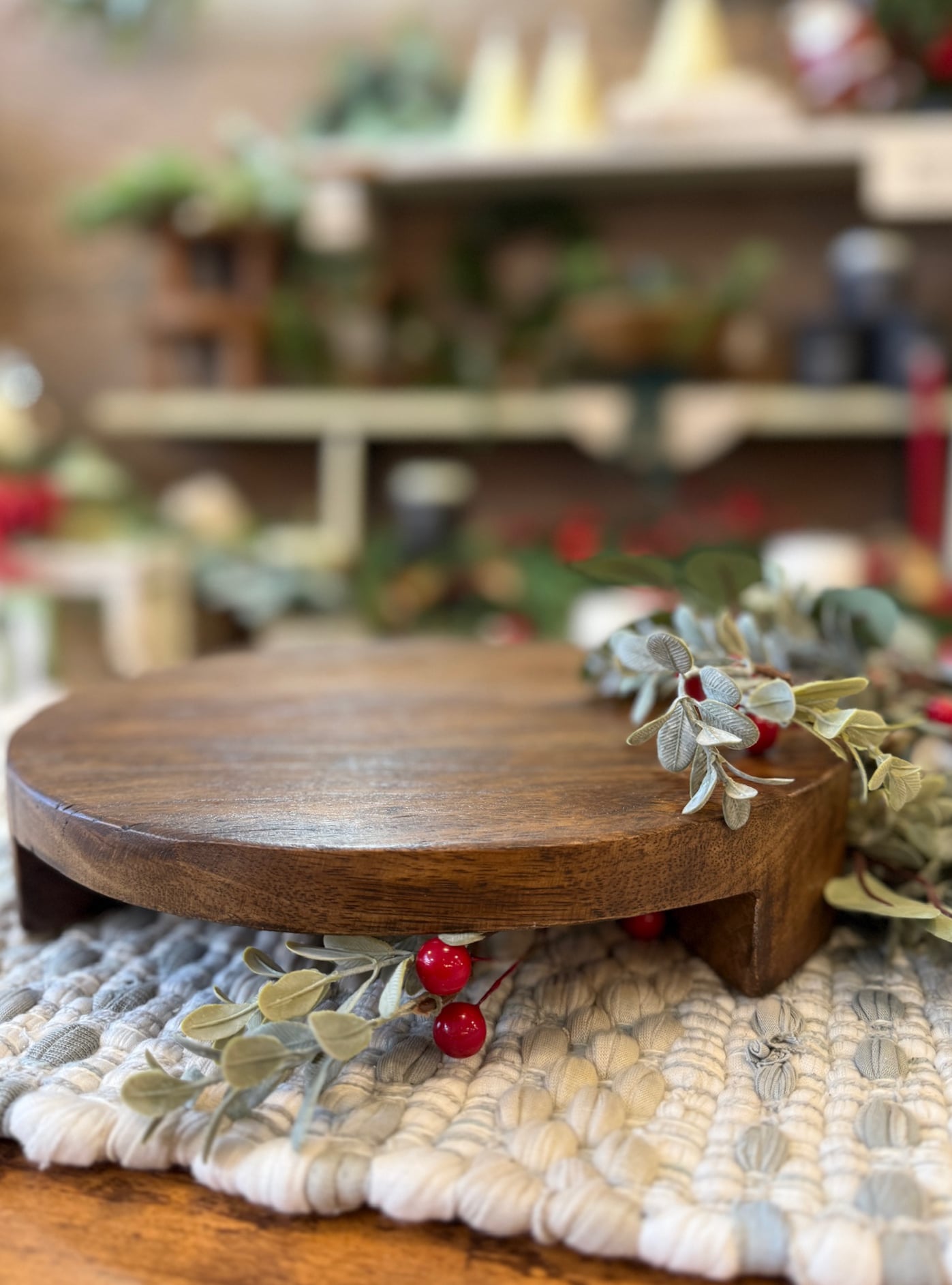 Side-angle view of a large wooden pedestal with warm grain, surrounded by greenery accents.