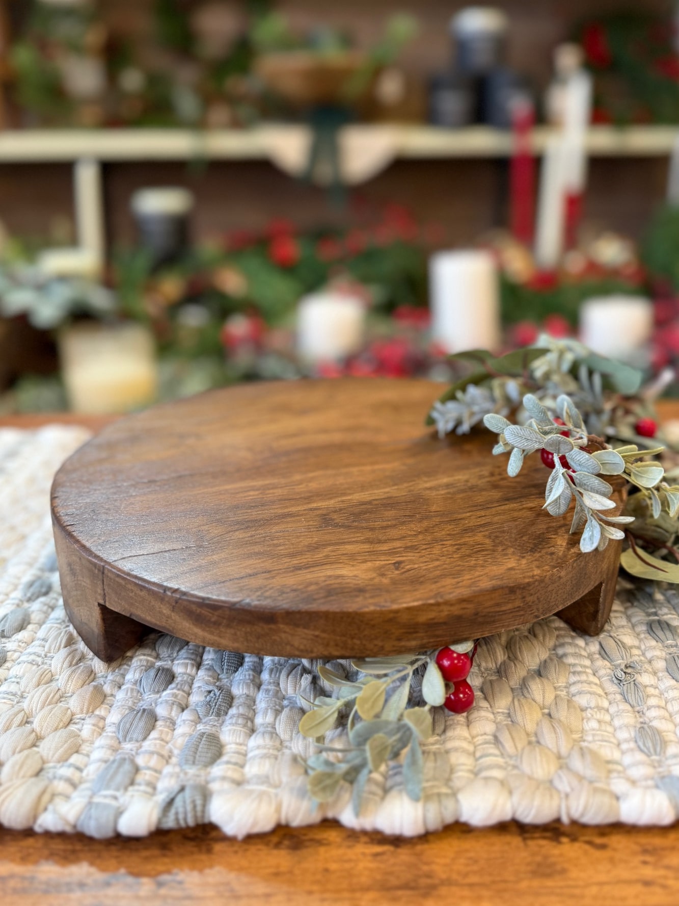 be-made-hays-ks-found-wood-pedestal-large Large round found wood pedestal styled on a woven mat with greenery and red berries.