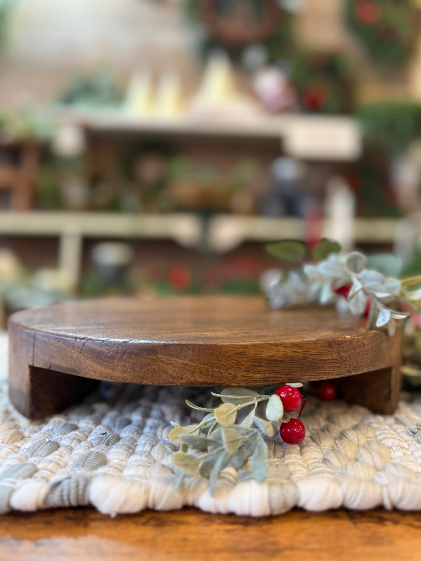 Side angle of a medium round wood pedestal elevated on carved feet surrounded by greenery.