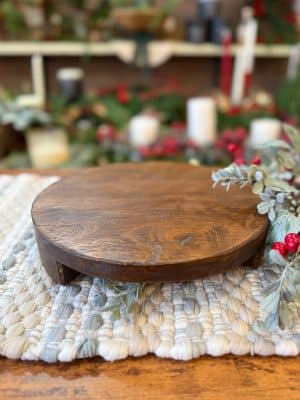Medium round found wood pedestal styled on a woven mat with greenery and red berries.