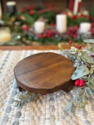 Handcrafted small wooden pedestal displayed on a textured neutral mat with holiday greenery.