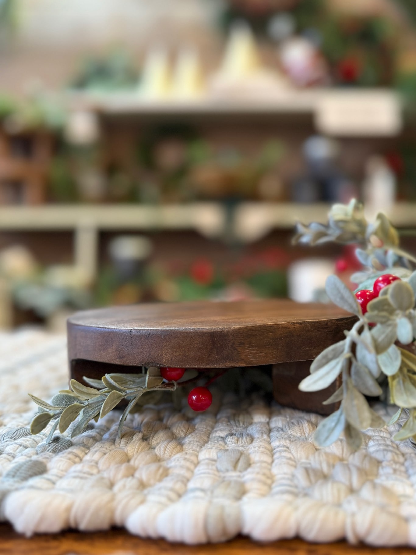 Small round found wood pedestal styled on a woven mat with greenery and red berries.