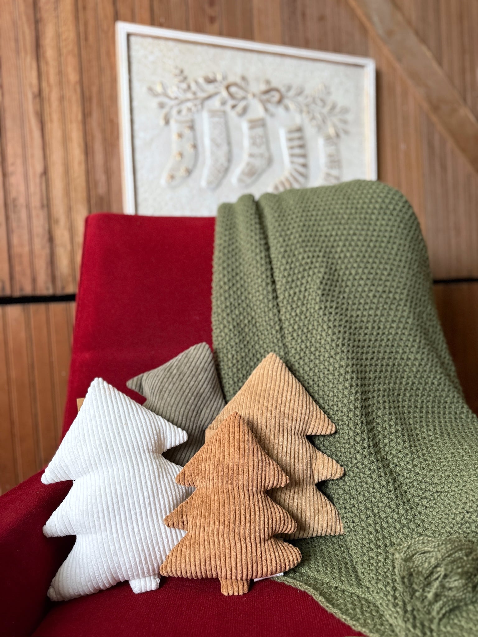 Corduroy stuffed tree pillows in neutral tones styled on a red chair with an olive green tassel throw blanket draped over the back.
