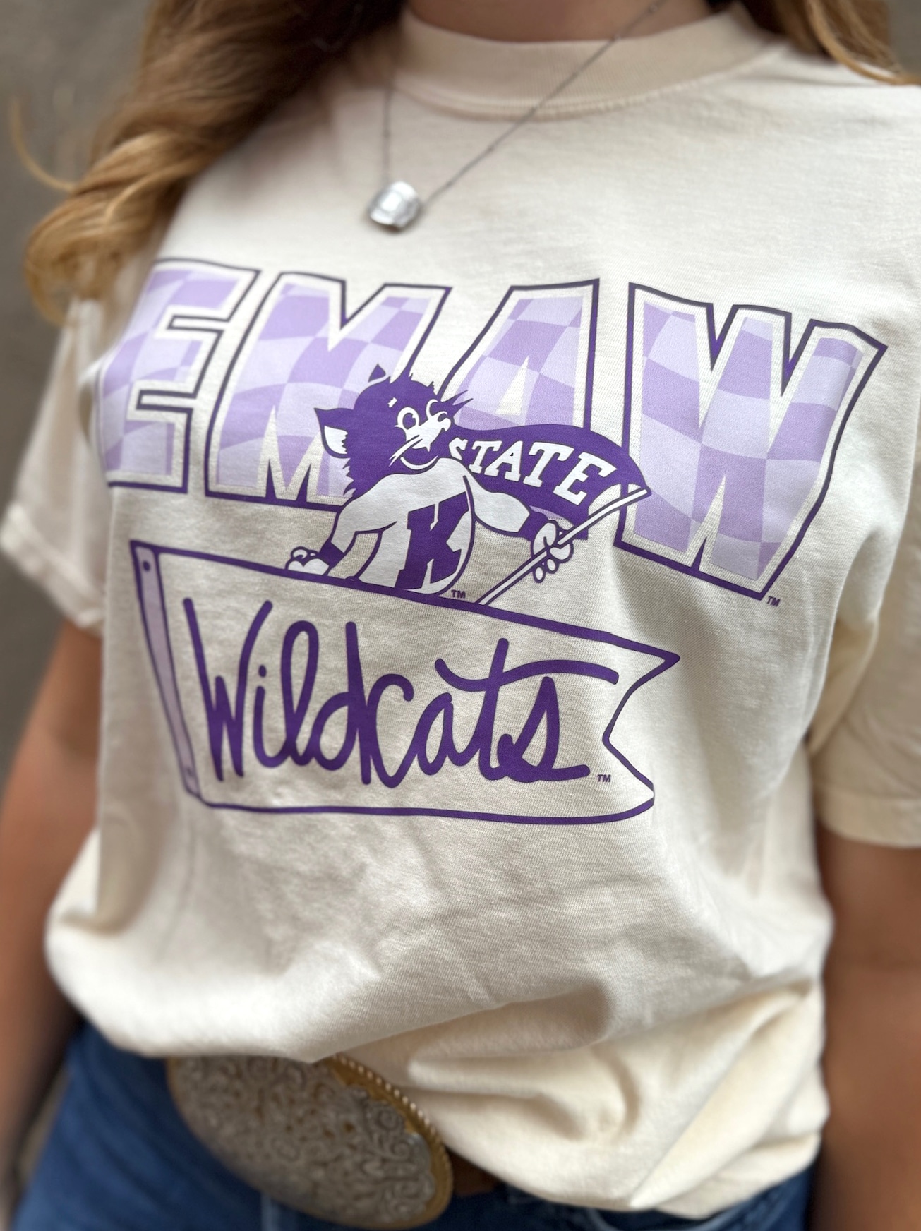 Close-up of ivory EMAW Wildcats tee featuring purple mascot graphic and relaxed unisex fit.