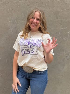 Smiling fan in EMAW Wildcats ivory tee showing K-State spirit in purple and white.