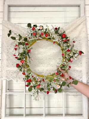 Garden-inspired pink and greenery wreath with gold ring base displayed on white paneled wall.