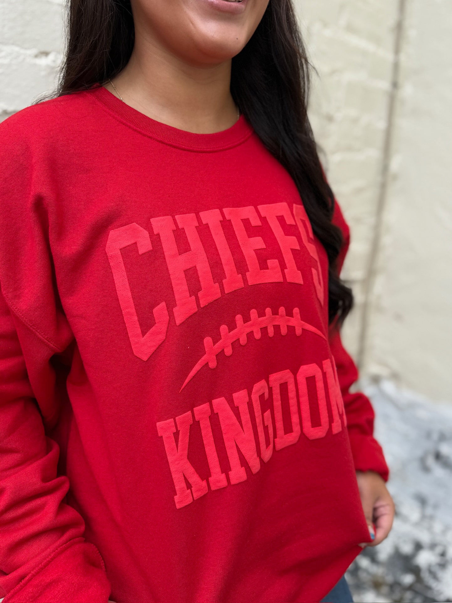 Close-up of Chiefs Kingdom crewneck in red with puff ink lettering and football detail.