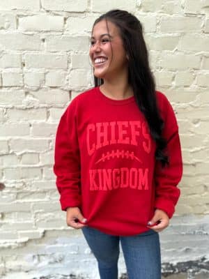 Woman smiling in red Chiefs Kingdom puff ink crewneck with raised monochrome design.