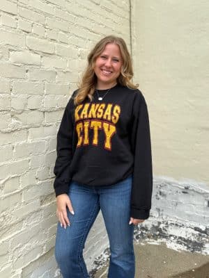 Woman wearing a black Kansas City Block Crewneck with bold red and gold lettering, styled with denim for a casual game day look.