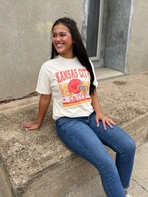 Woman smiling in ivory Chiefs vintage graphic tee with bold red helmet and gold lettering.