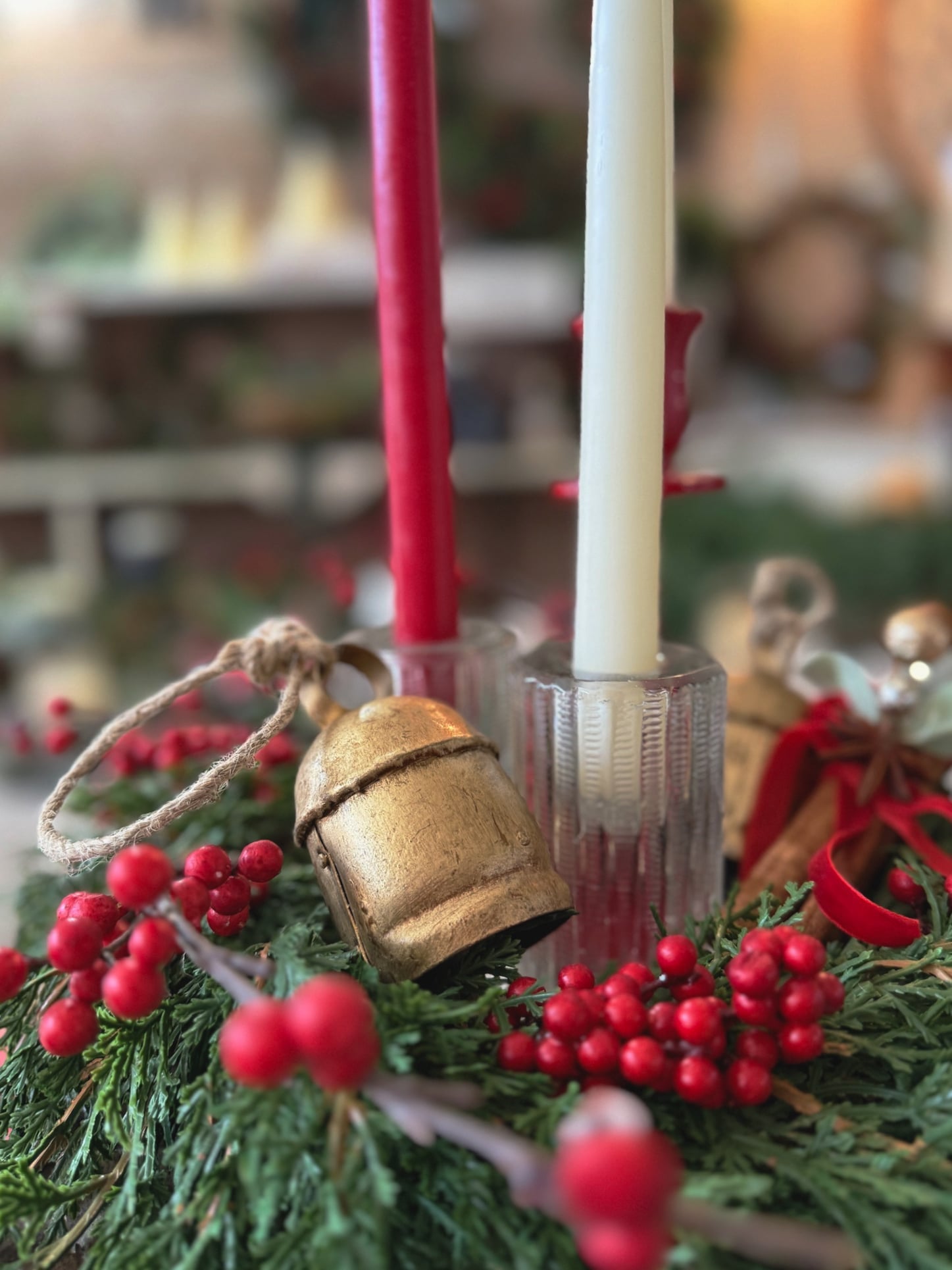 Cut glass taper candle holder styled in a Christmas wreath with red berries, gold bell, and red and white taper candles.