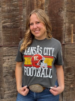 Woman wearing Kansas City Football Graphic Tee in pepper color with distressed red helmet and gold stripes. Printed on a Comfort Colors tee in the shade Pepper, this shirt has the ultra-soft, washed cotton feel that only gets better with wear. Designed with a relaxed unisex fit, it’s perfect for pairing with denim, joggers, or leggings whether you’re tailgating at Arrowhead, watching from home, or celebrating Red Friday around town. Style: Unisex Graphic Tee Brand: Comfort Colors Color: Pepper (washed charcoal tone) Print: Distressed Kansas City Football design with red KC helmet and block lettering Fit: Relaxed, true-to-size unisex fit Material: 100% Cotton