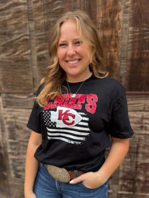 Close-up of black Chiefs tee with distressed CHIEFS lettering, KC arrowhead, and American flag backdrop.
