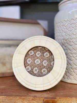Round bone photo frame with hand-carved detailing, styled on a wood shelf with neutral décor.
