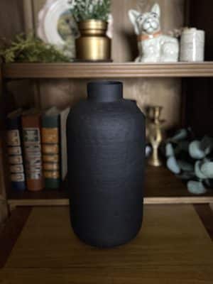 Close-up of the Textured Oblong Vase – Large in matte black, displayed on a wooden shelf beside books and decor.