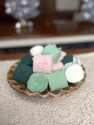 Chiffon ribbon rolls in green, mint, pink, and cream displayed in a carved wood bowl for crafting and gift wrapping.