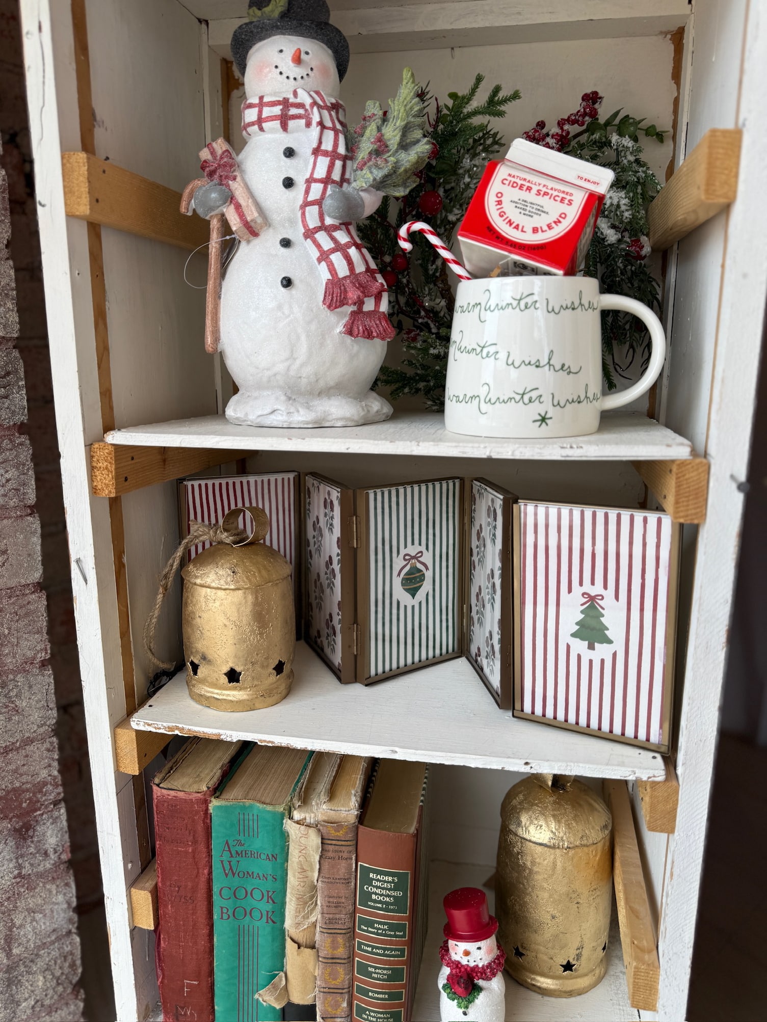 Oversized hinged gold photo frame displayed on a white shelf with holiday décor, books, and gold bells.