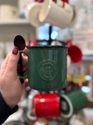 Front view of green “Santa Certified” ceramic mug with embossed stamp and spoon in handle.