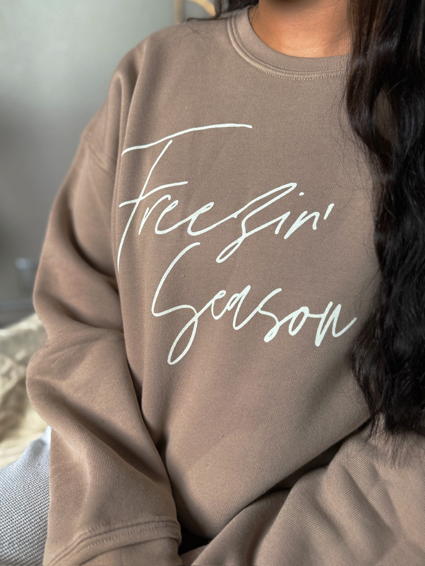 Close-up of Freezin’ Season script graphic on tan crewneck pullover