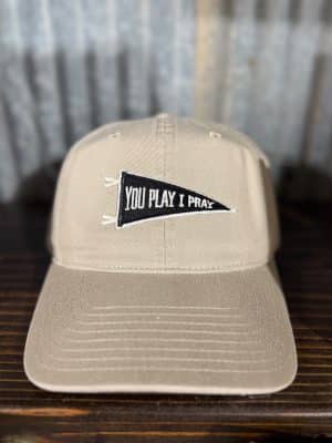 Front-close view of tan baseball cap with black “You Play I Pray” pennant patch
