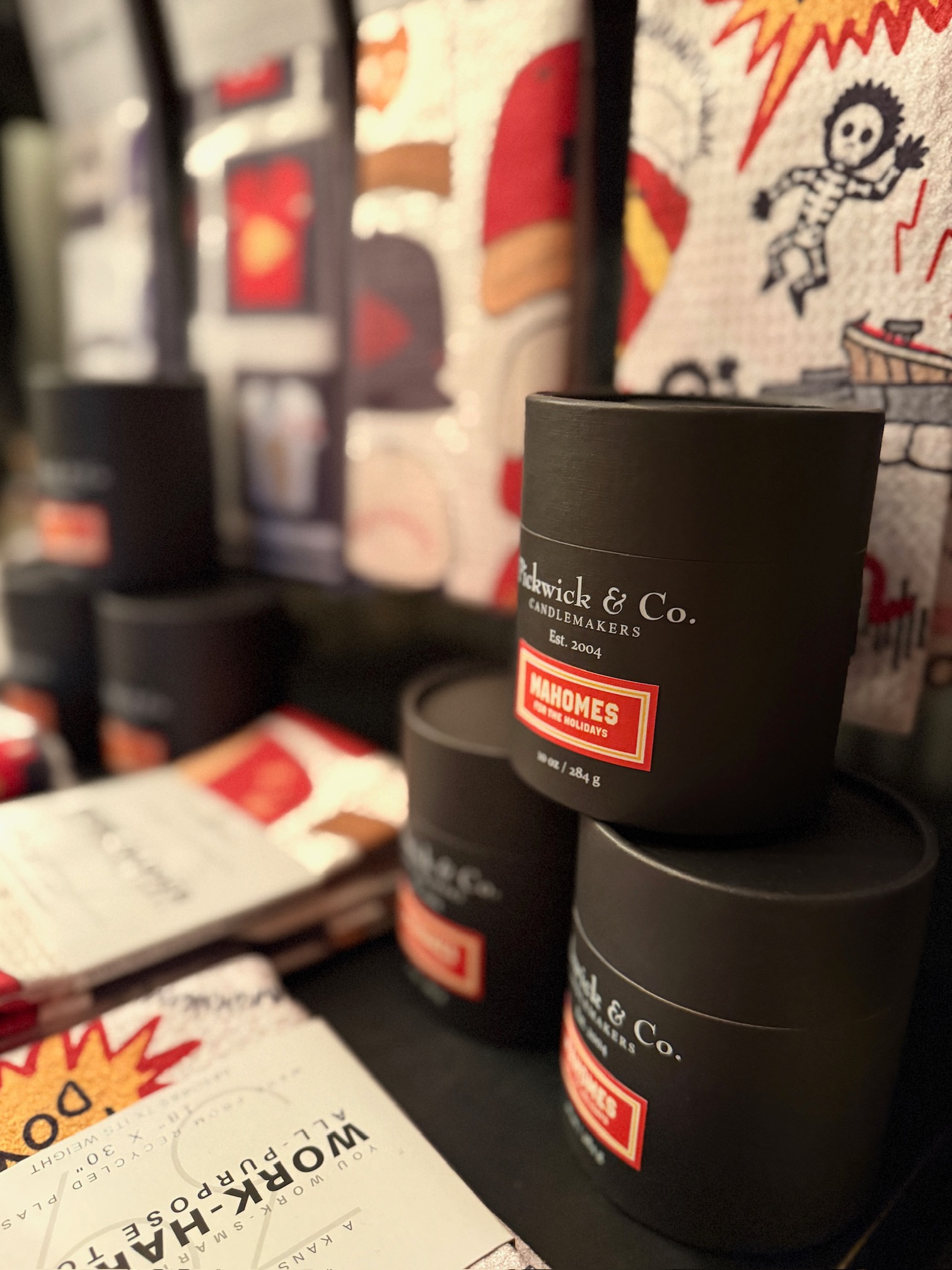 be-made-hays-ks-pickwick-mahomes-for-the-holidays-candle Pickwick & Co. Mahomes for the Holidays candle in sleek black packaging displayed with festive kitchen towels and gifts, featuring the signature red label.
