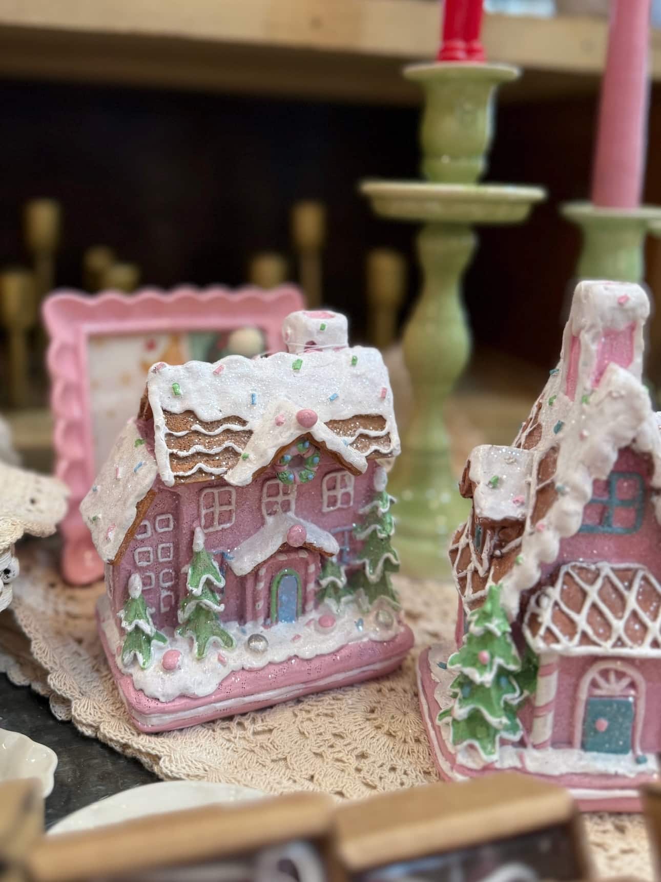 Pink gingerbread houses with frosted rooftops styled together with candlesticks in the background.