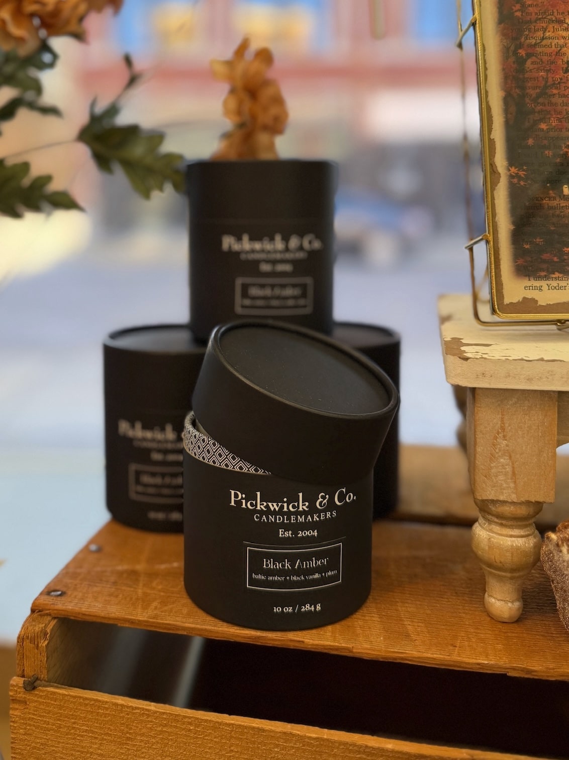 be-made-hays-ks-black-amber-pickwick-candle-10oz Black Pickwick & Co. Black Amber candle displayed on a wooden shelf with elegant packaging and warm-toned decor in the background.