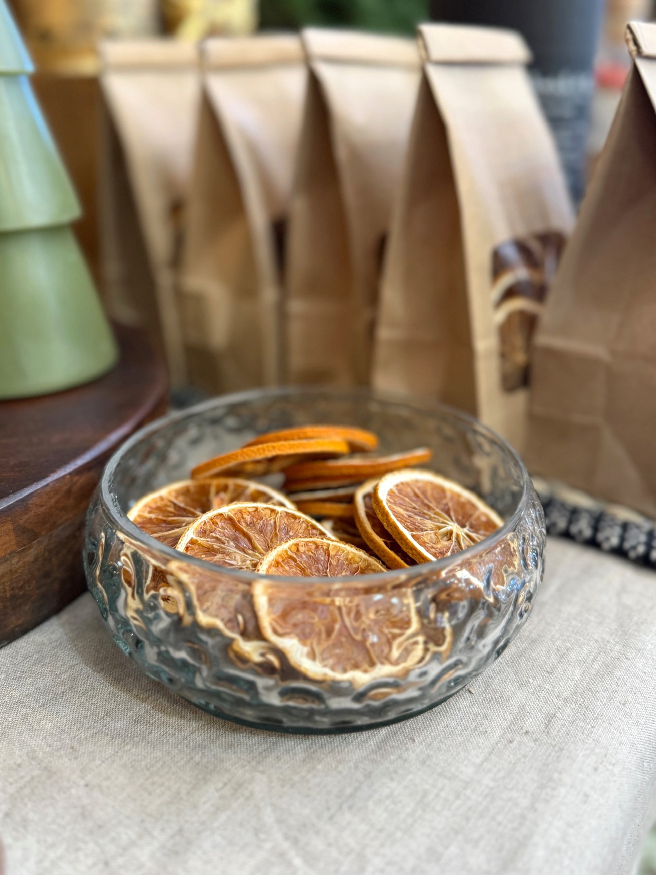 Clear hobnail glass bowl filled with dried orange slices, styled with kraft bags in the background.