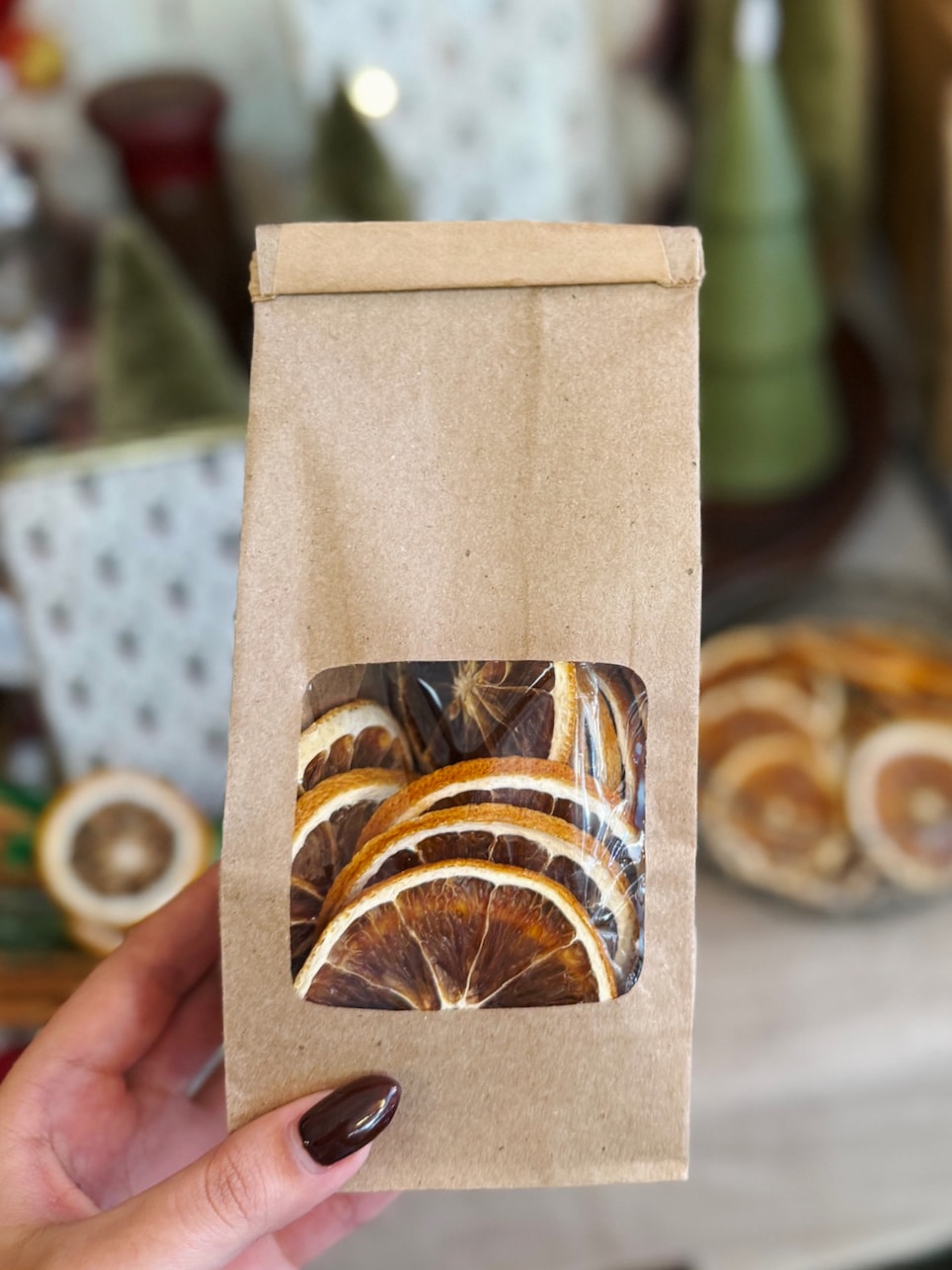 Dried orange slices in a brown kraft bag with a clear window showing the citrus pieces inside.