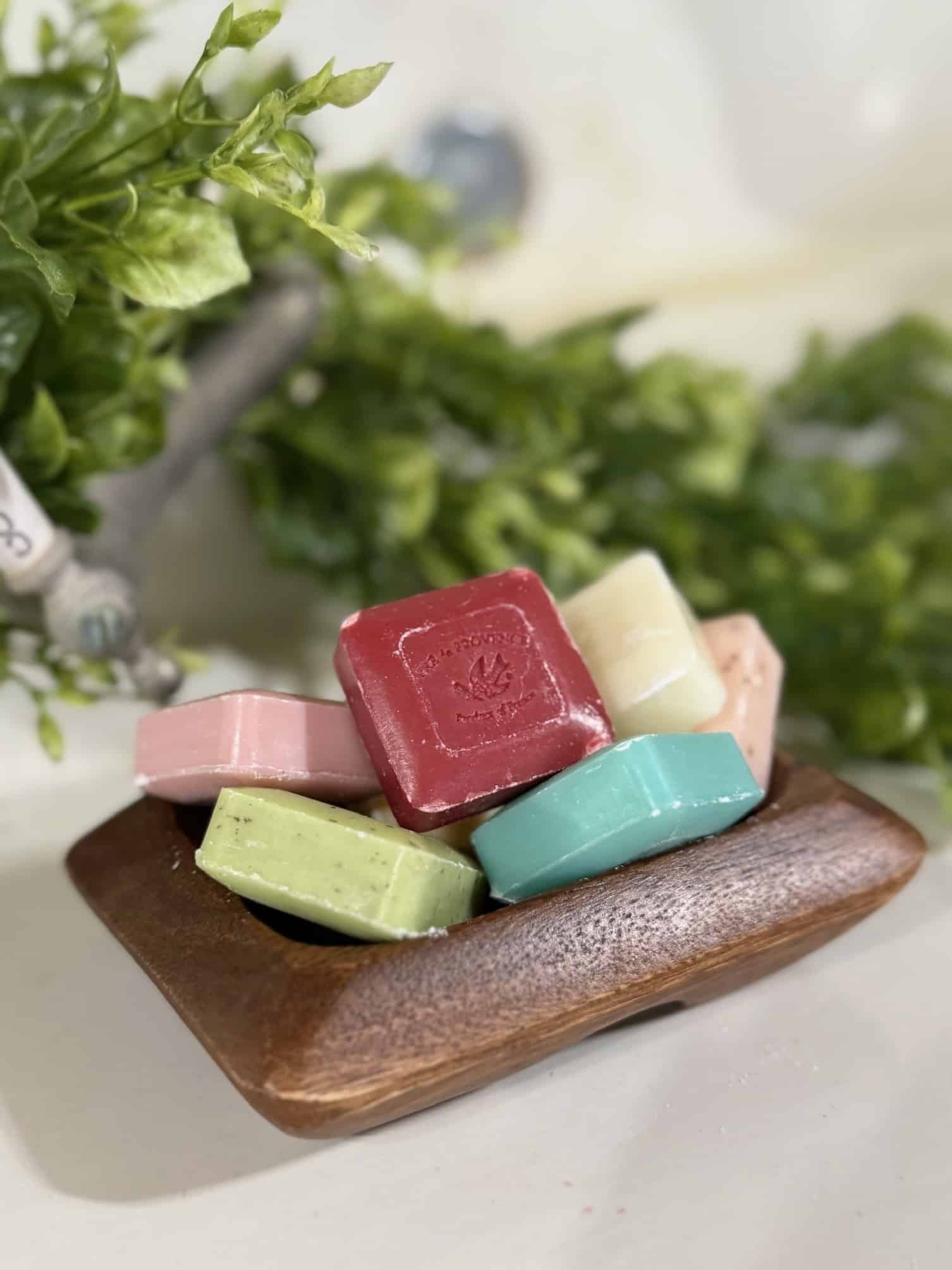 Acacia wood soap dish holding assorted colorful French-milled mini bar soaps.