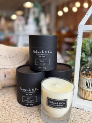 Hotel Pickwick Candle – 10 oz displayed with its black box and glass vessel on a textured surface