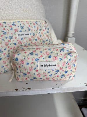 Small quilted corduroy floral makeup bag with beige lining and zipper displayed on white chair.