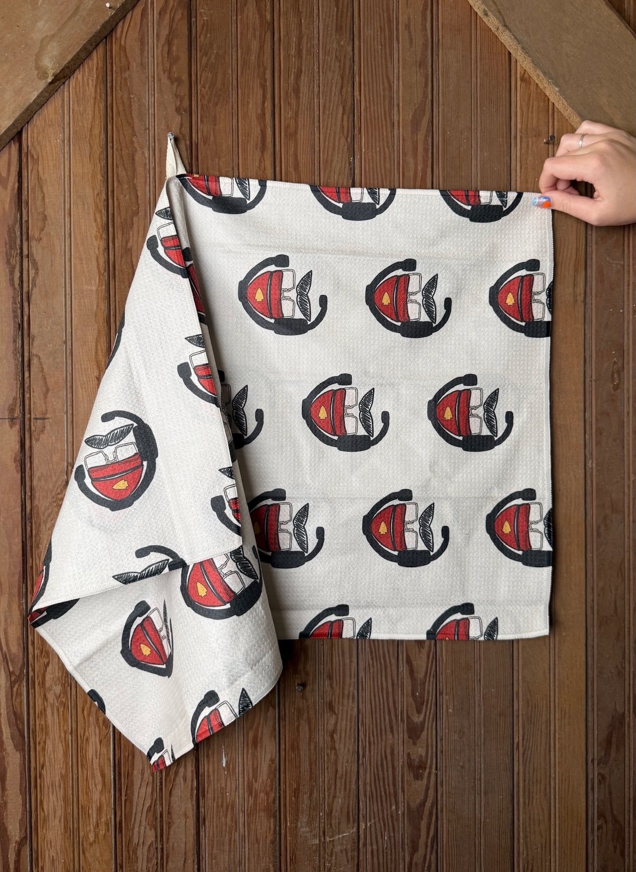 KC Chiefs Big Red Tea Towel featuring a repeating red cap and headset design, shown hanging and folded on a wooden surface.