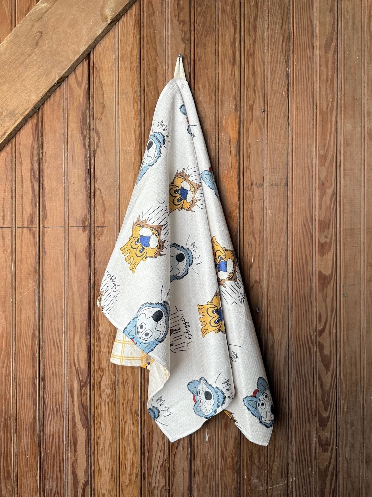 be-made-hays-ks-royals-chiefs-mascot-tea-towel Double-sided Kansas City Mascot Tea Towel featuring KC Wolf and Sluggerrr character prints, hung neatly against wood paneling.