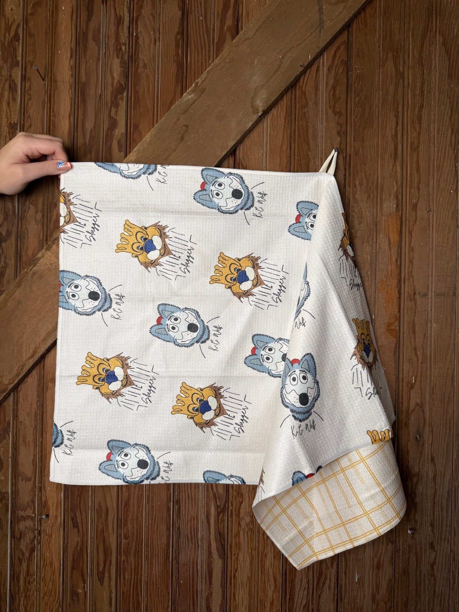 KC Chiefs & Royals Mascot Tea Towel featuring cartoon sketches of KC Wolf and Sluggerrr on white microfiber fabric, displayed hanging on a wood background.