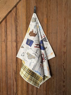 Double-sided Kansas Icons Tea Towel featuring colorful sketches of state symbols and patterns, draped on a wooden wall.