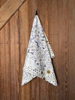 Double-sided KSU Tea Towel with “Eat ’Em Up” center artwork and tailgate motifs on one side and bright sunflower pattern on the reverse, shown hanging on wood panel wall.
