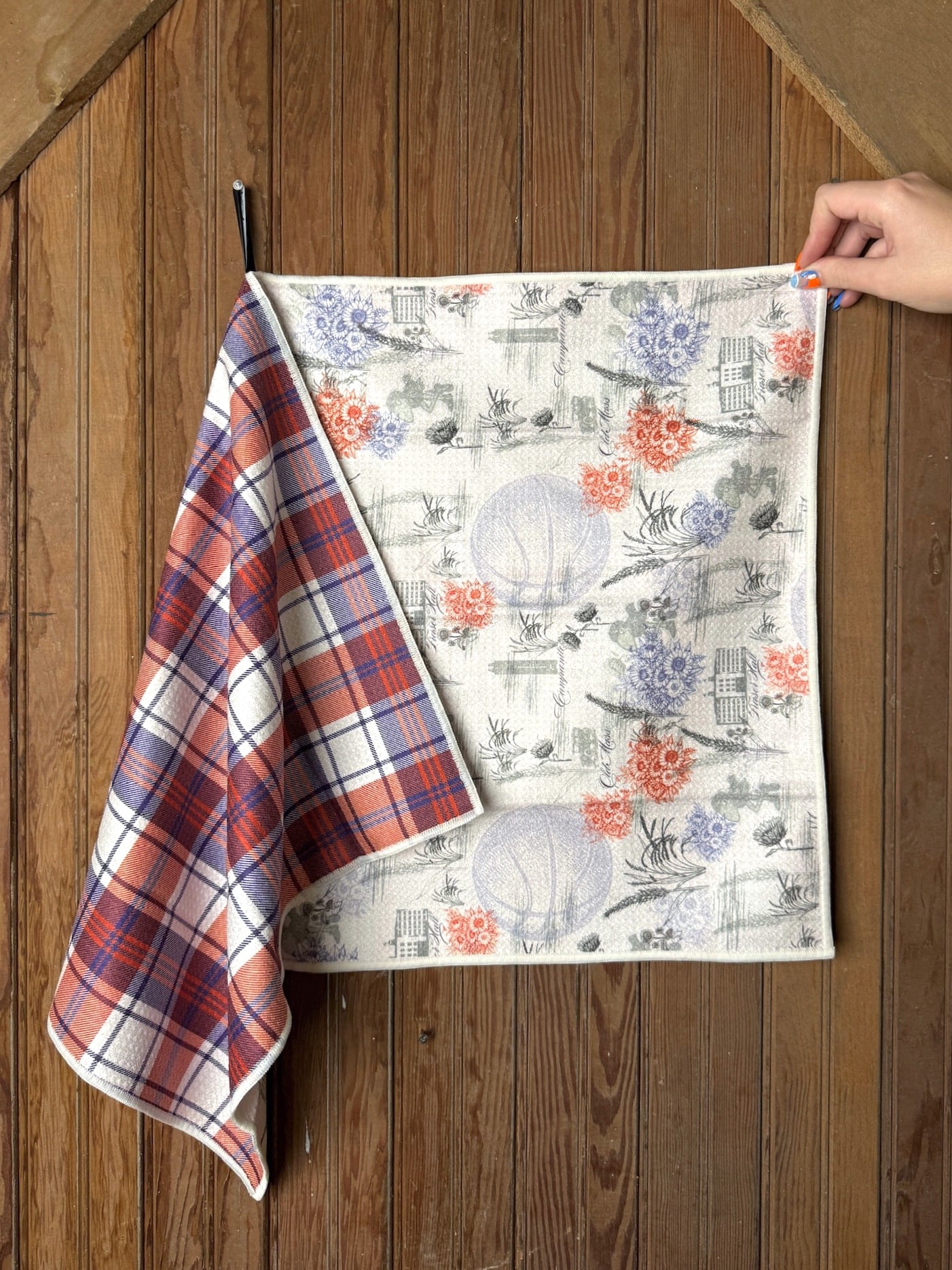 KU 1912 Basketball Tea Towel displayed flat to show the red-and-blue plaid reverse and vintage-style KU landmark print with florals and basketball sketches.