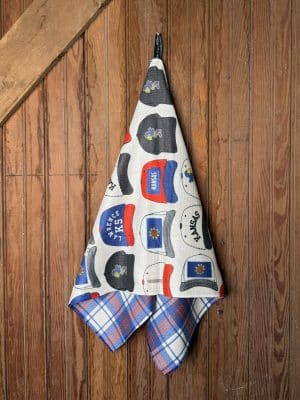 Full hanging view of KU Hats Tea Towel featuring illustrated Jayhawk-inspired hats with “Kansas,” “Lawrence,” and KU graphics in red and blue.