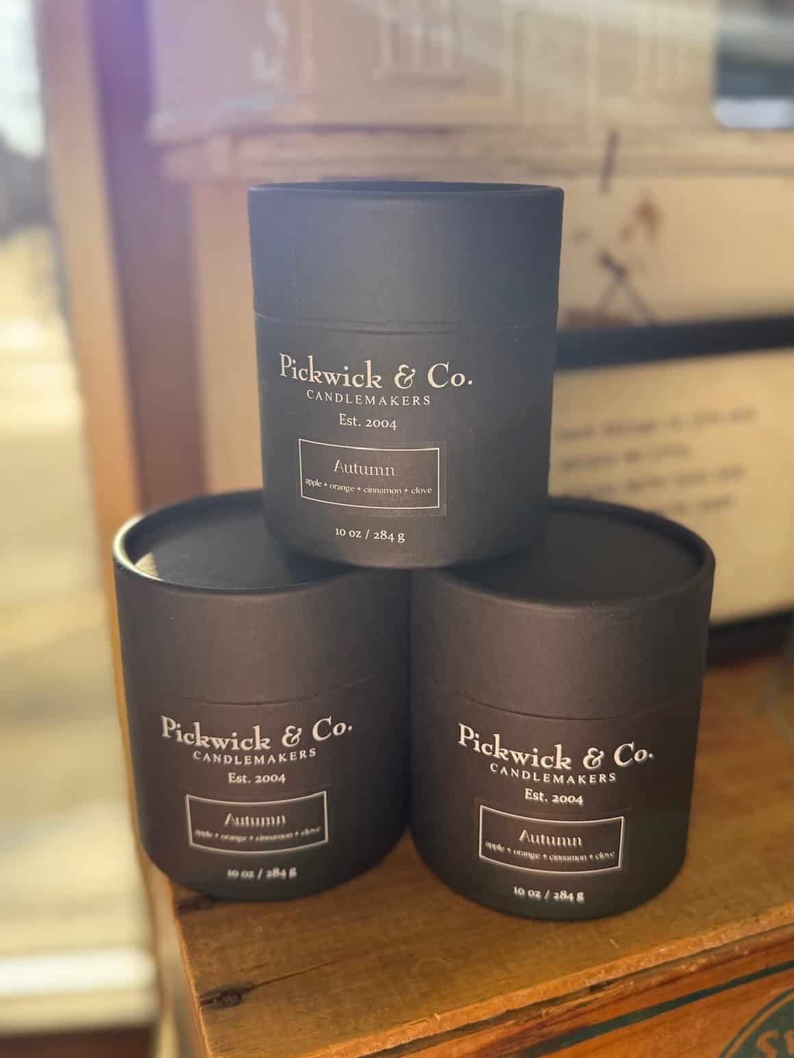 be-made-hays-ks-autumn-pickwick-candle-10oz Three black Pickwick & Co. Autumn candles stacked on a wooden shelf, featuring sleek black packaging and a warm seasonal fragrance of baked apple, orange peel, cinnamon, and clove.