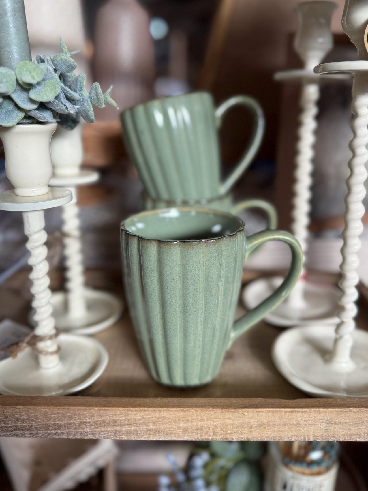 Sage green ribbed stoneware mugs displayed on a wooden tray surrounded by cream candlesticks and greenery.