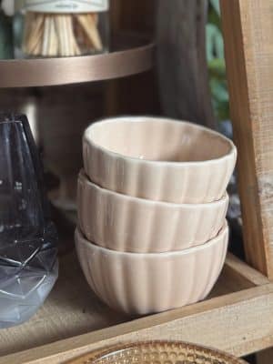 Stack of three cream ribbed stoneware bowls with a reactive glaze finish styled on a wooden shelf.