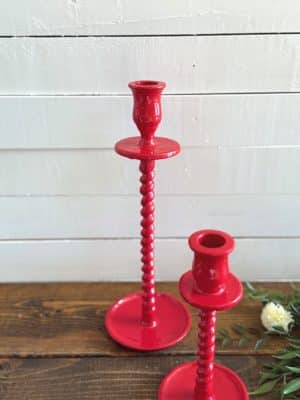 Red corkscrew taper candle holders on stacked books with greenery and a shiplap background